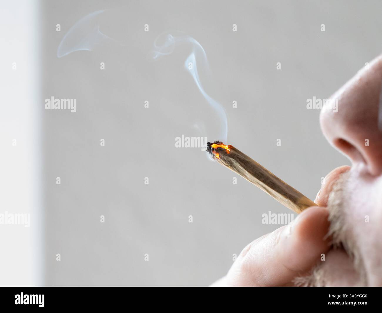 Fumare un primo piano. Inalare il fumo di una sigaretta con la cannabis. Un giovane tiene il fusto luminoso in bocca e lo sta godendo. Foto Stock