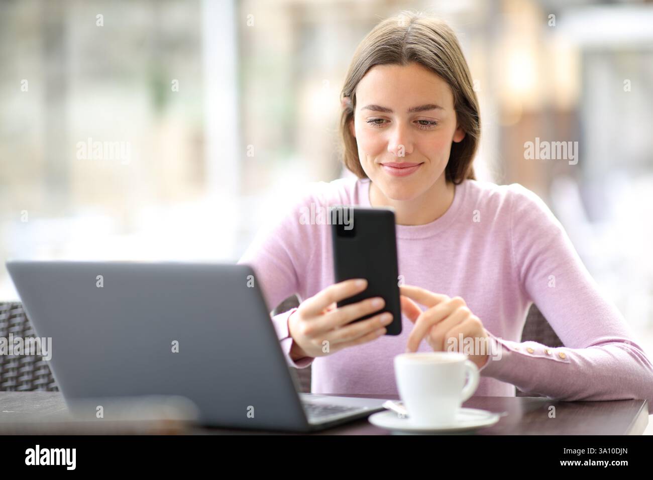 Donna soddisfatta in un bar che utilizza più dispositivi che controllano telefono e laptop Foto Stock