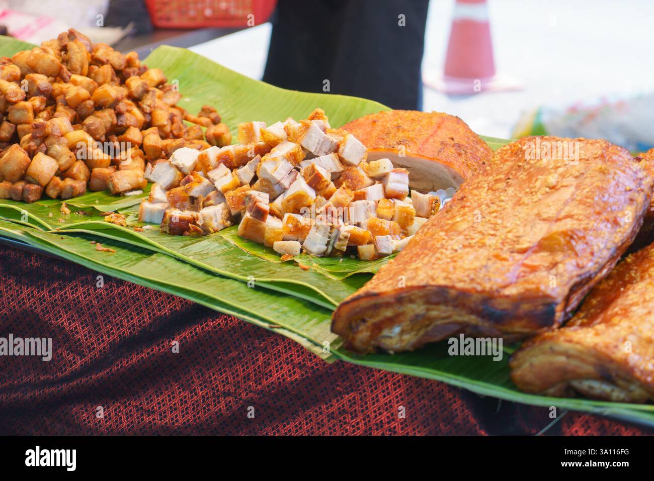 primo piano di croccanti fette di pancetta di maiale e bocconcini di maiale fritti ordinatamente disposti su foglie di banana in uno stand di street food. Foto Stock