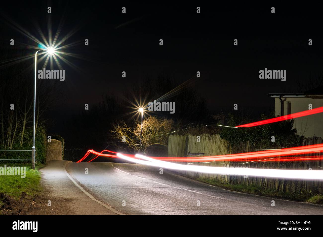 Una strada ai margini della campagna con sentieri e semafori di notte Foto Stock