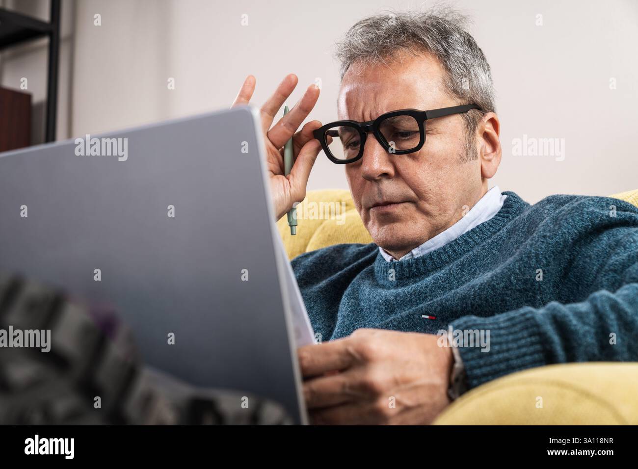 Primo piano di un uomo anziano che indossa occhiali, molto concentrato durante la lettura e l'analisi di documenti su un notebook. Concetto di strategia aziendale, lavoro remoto, Foto Stock