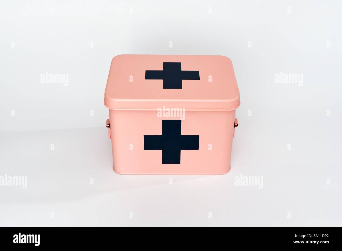 L'immagine mostra una cassetta di pronto soccorso rosa con croci nere sulla parte superiore e anteriore. È posizionato su un semplice sfondo bianco, enfatizzando la sua c Foto Stock