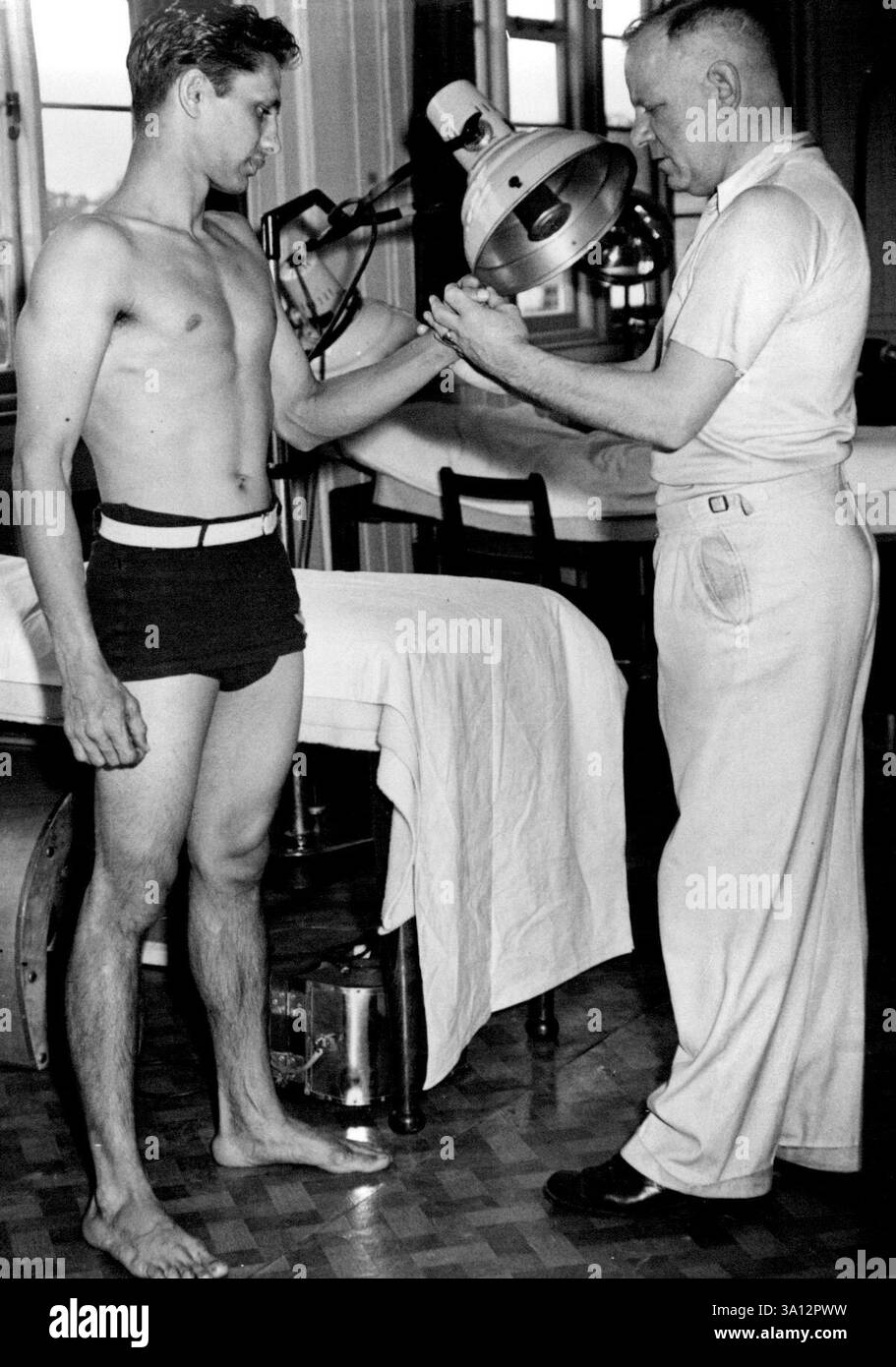 La vita nel "Villaggio Olimpico". Atleti provenienti da tutto il mondo si stanno riunendo in Inghilterra per la XIV Olimpiade. Gli uomini si trovano in tre "Village" - Richmond Park, Uxbridge e West Drayton, mentre le donne hanno il loro alloggio al Southlands College, Wimbledon, tutti a breve distanza dal centro di Londra. Nella sala massaggi del 'Olympic Village' Richmond Park. Sig. E.T.W . Raikes, capo massaggiatore, che tratta Eddie Gray, campione di pugilato leggero. 18 luglio 1948. (Foto di Sport & General Press Agency, Limited). Foto Stock