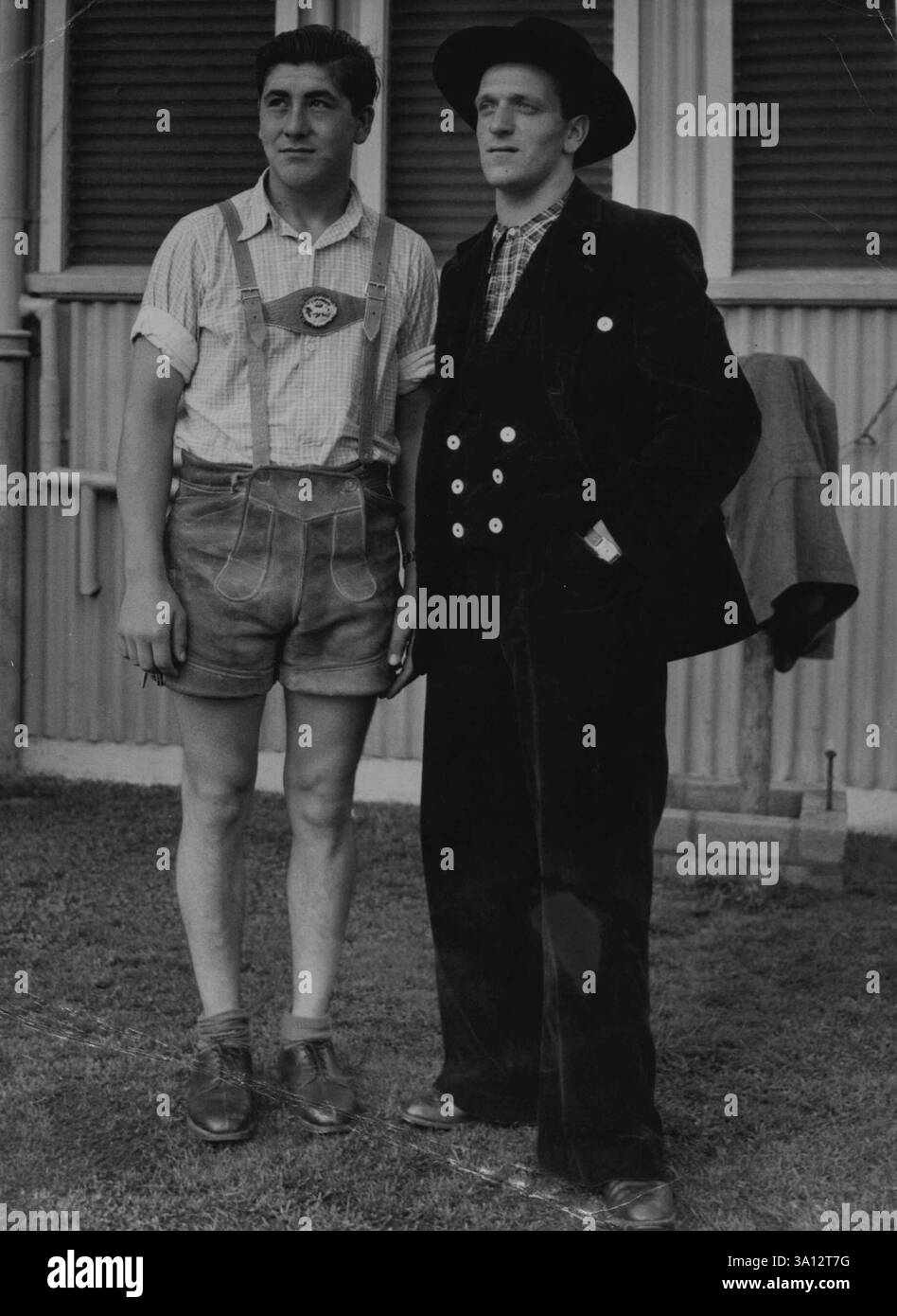 Oggi, Out Weather non ha impressionato Walter Rush, 20 anni, di Francoforte (a sinistra) - pantaloncini - che ha fatto un sorprendente contrasto con Matthaud Schetter, 19 anni, di Wurttemburg, quando hanno raggiunto Sydney con BOAC Constellation indossando costumi tradizionali tedeschi nazionali. Lavoreranno sul progetto Tasmanian Hydro Electric. 28 giugno 1951. Foto Stock