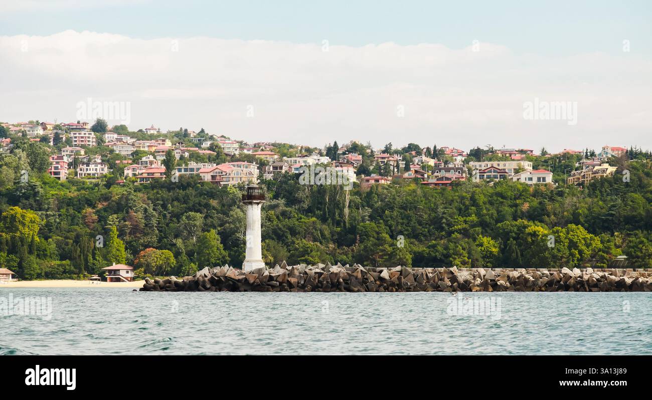 Splendido villaggio costiero circondato da lussureggianti alberi verdi, caratterizzato da un faro e acque tranquille. Ideale per temi marittimi, tranquillità, natura, su Foto Stock