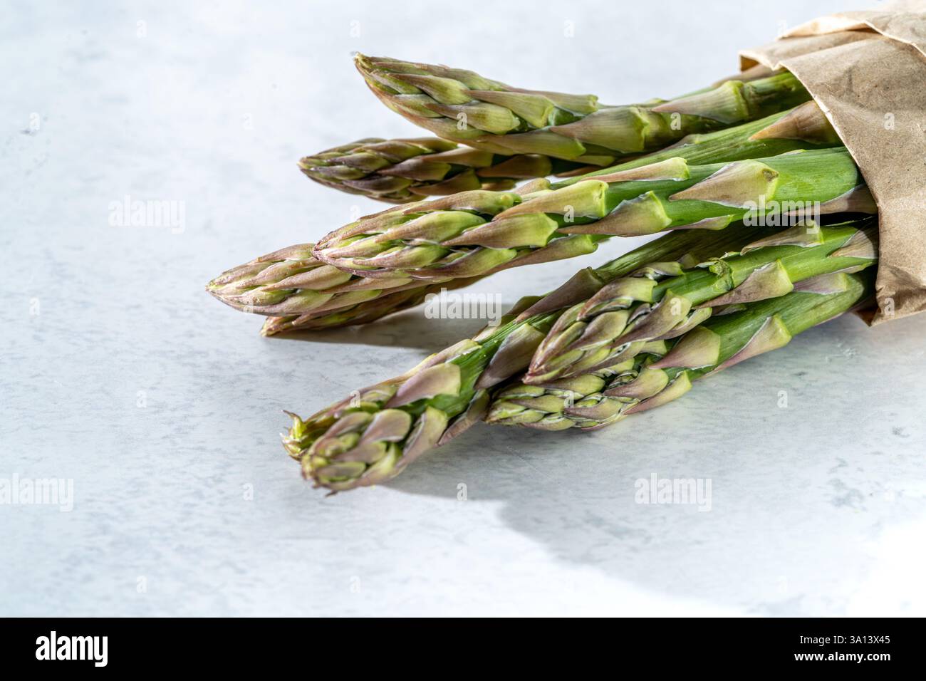 fascio di asparagi verdi in sacchetto di carta su marmo di pietra bianca, vista ad angolo elevato, direzione diagonale da destra, primo piano, spazio di copia Foto Stock
