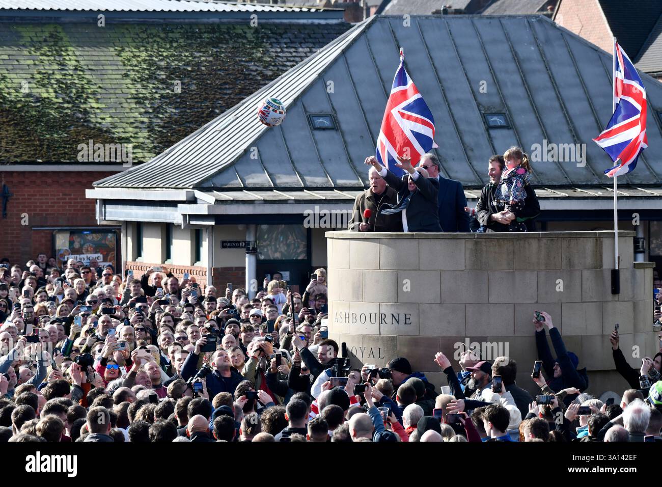 Ashbourne Royal Shrovetide, antica partita di baseball con il contadino locale David Bott che alza il pallone sul basamento del centro città. Foto Stock