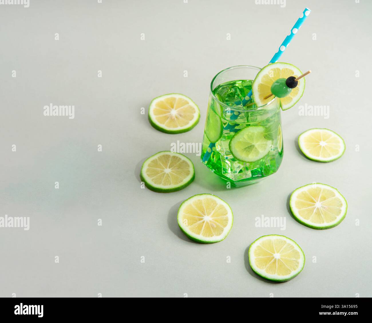 Cocktail alla menta guarnito con fetta di limone, sherbet blu e ciliegia verde circondato da fette di limone sul tavolo bianco Foto Stock