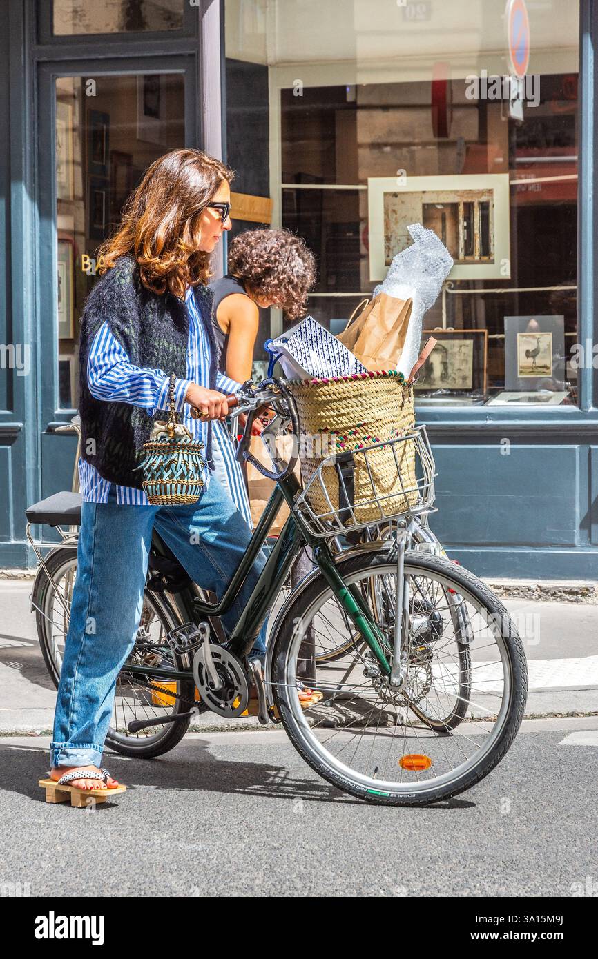 Due giovani donne alla moda che partono su biciclette carichi di shopping in Rue du Dragon, Parigi 75006, Francia. Foto Stock