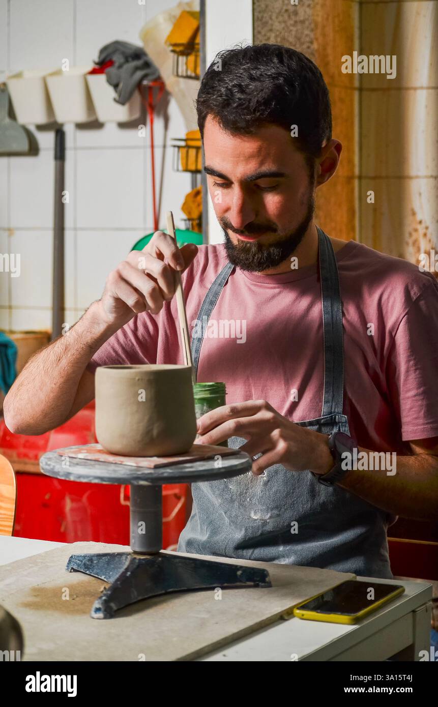 Artigiano che lavora con l'argilla in un laboratorio di ceramica, levigando una pentola di argilla con uno strumento di legno Foto Stock