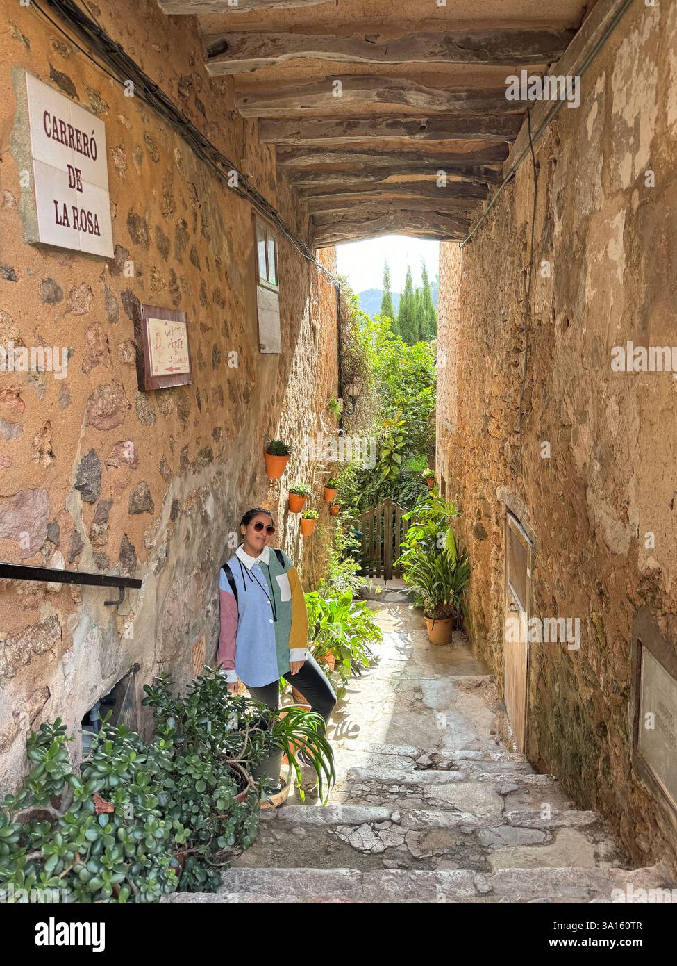 Una donna si trova in un vicolo stretto con un uomo dietro di lei. Il vicolo è fiancheggiato da piante in vaso e ha un cartello sul muro. La scena ha un senso Foto Stock