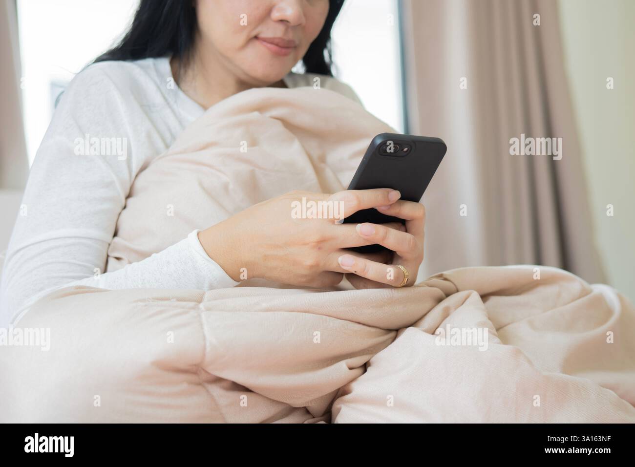 Donna asiatica anziana felice dopo il risveglio, guardando un film sdraiato sul letto in camera da letto a casa. Messa a fuoco selettiva. Foto Stock