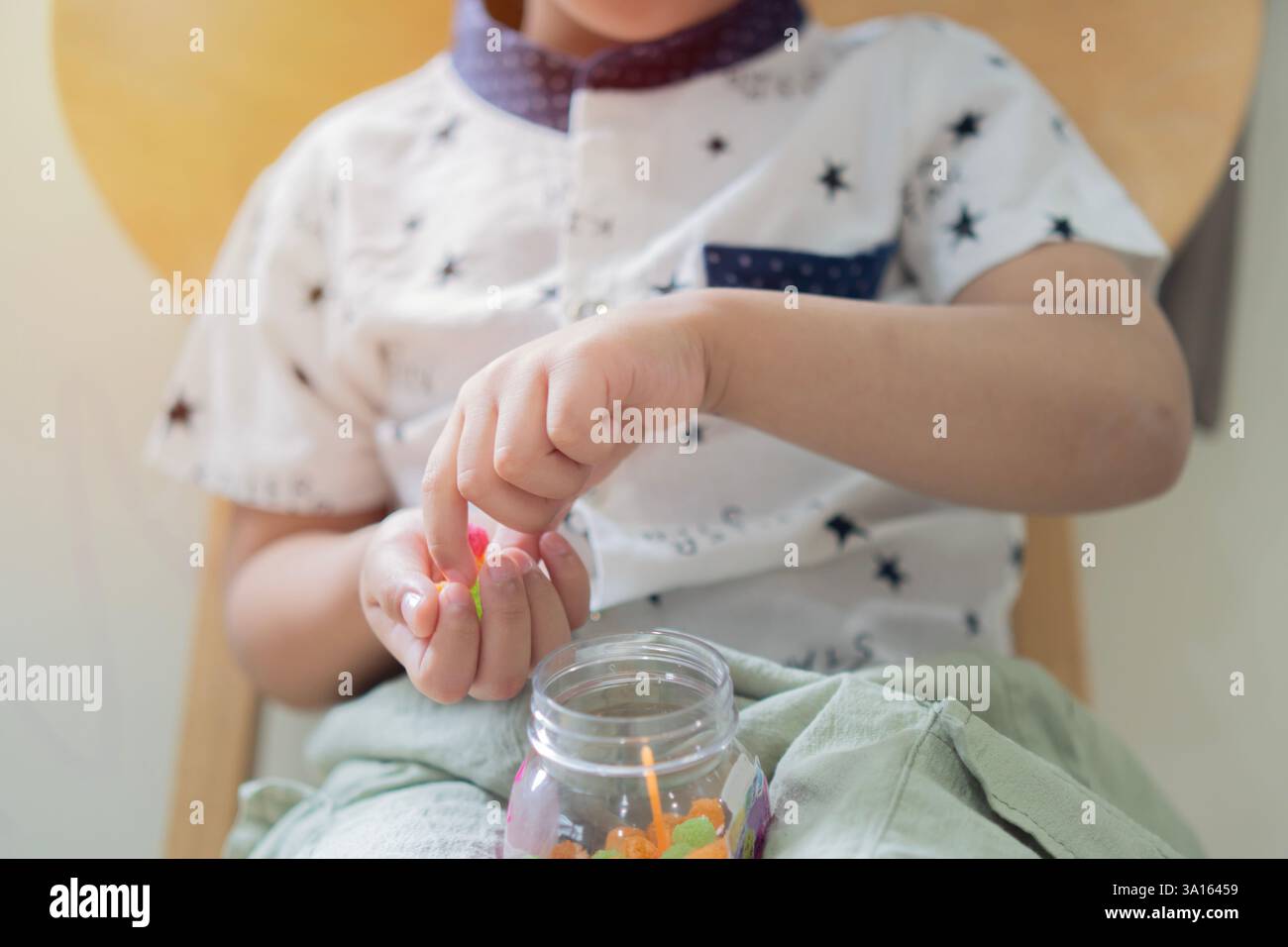 Il bambino si siede con le mani su una sedia di legno e tiene in primo piano caramelle colorate. Dolce spuntino per bambini. Foto Stock