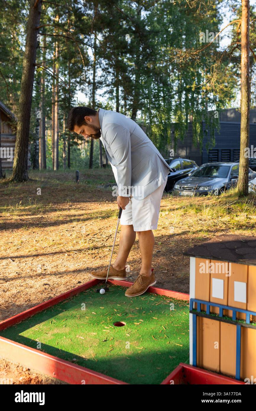 Elegante giovane adulto che gioca a minigolf su un campo forestale Foto Stock