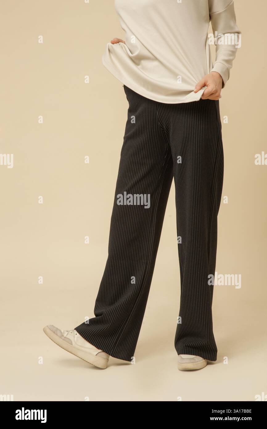 Modello femminile che indossa pantaloni a righe in bianco e nero e camicia bianca, foto da studio Foto Stock