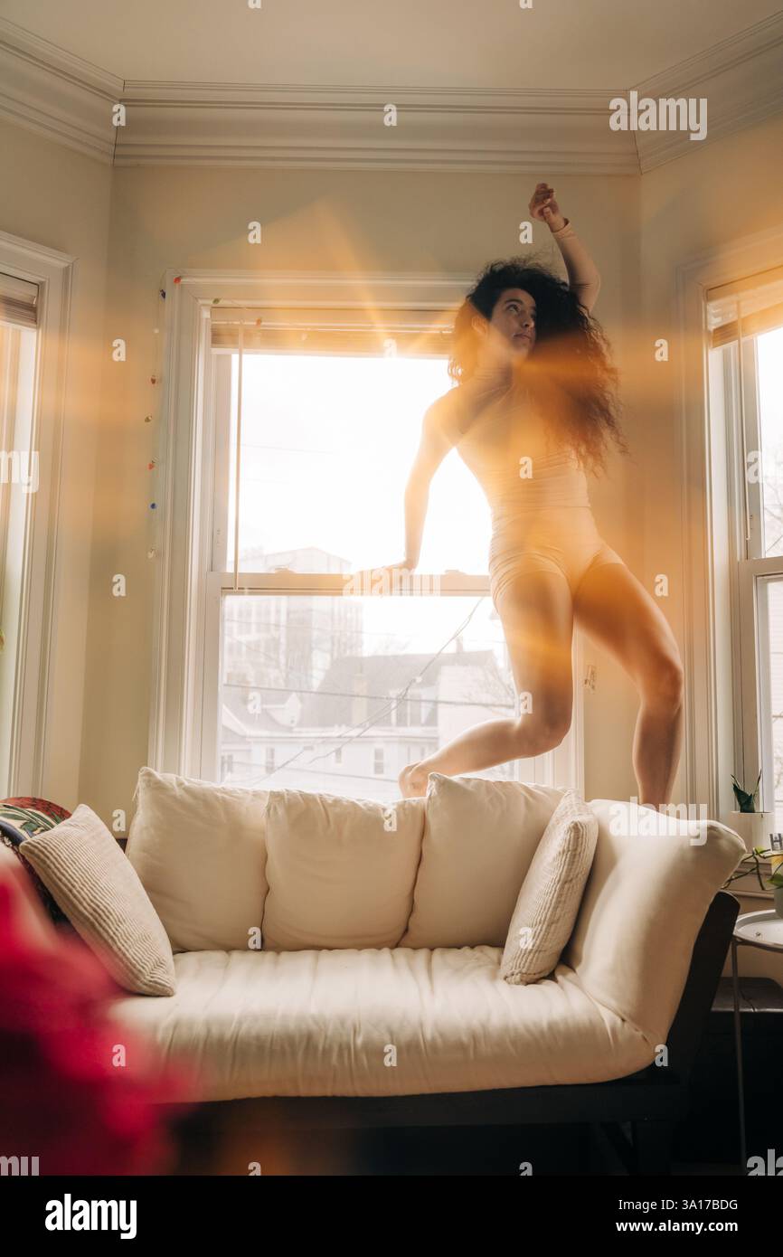 Donna che colpisce una posa espressiva vicino a una finestra illuminata dal sole Foto Stock