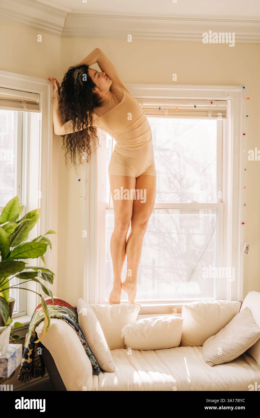 Donna in equilibrio elegantemente su un davanzale, bagnata dalla calda luce del sole Foto Stock