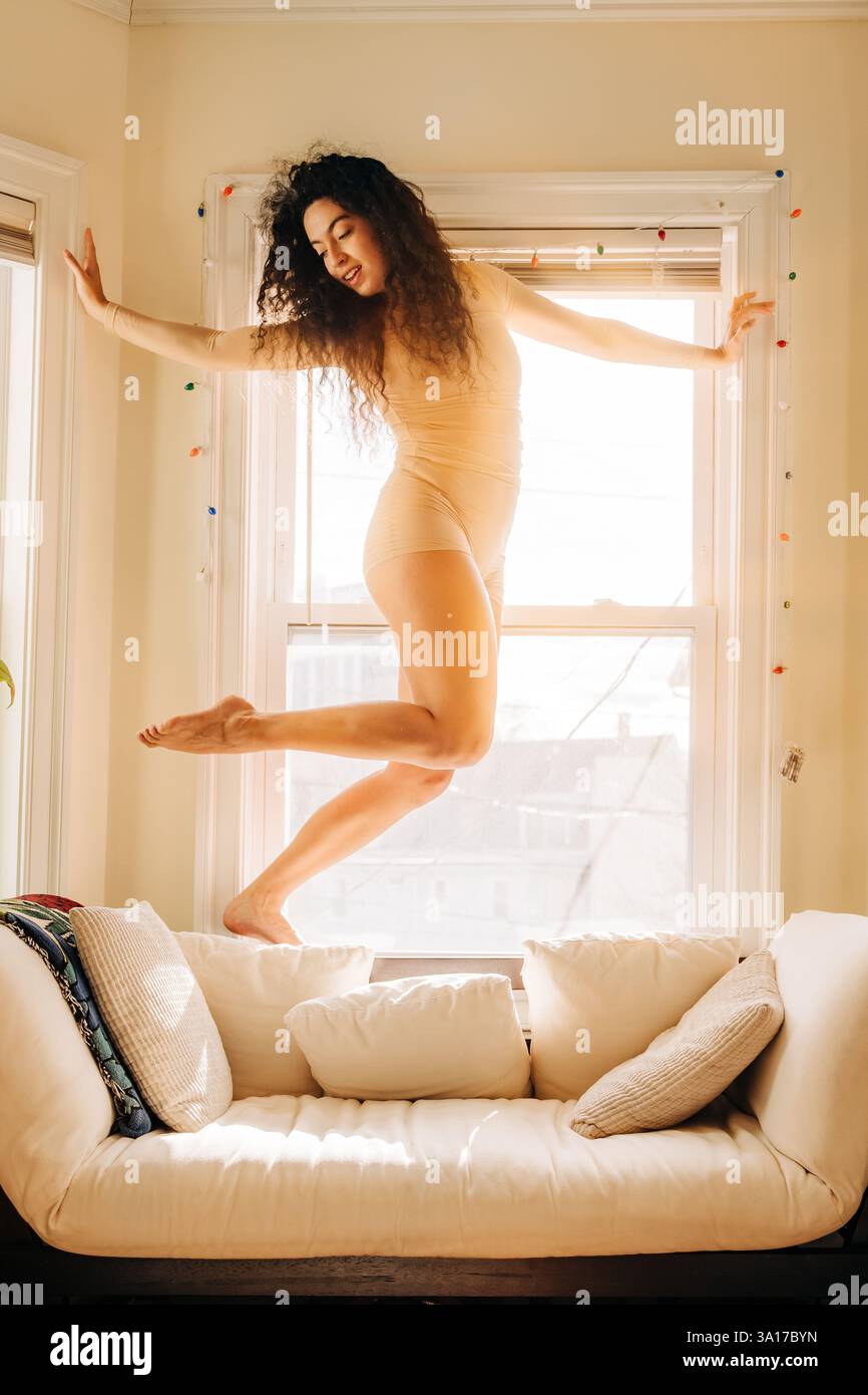 Donna in equilibrio elegantemente vicino a una finestra illuminata dal sole in una posa aggraziata Foto Stock