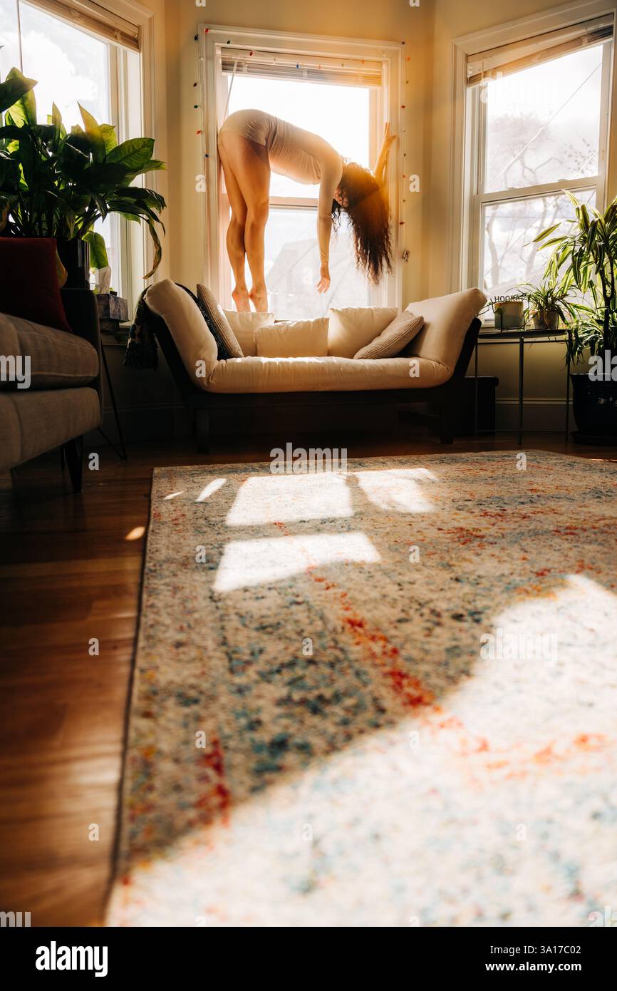La donna si piega graziosamente vicino a una finestra illuminata dal sole, gettando ombre morbide Foto Stock