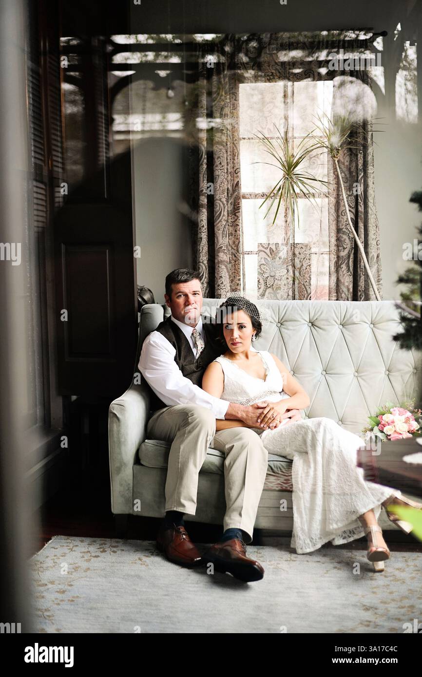 La sposa e lo sposo si siedono insieme su un divano vintage in un ambiente accogliente Foto Stock