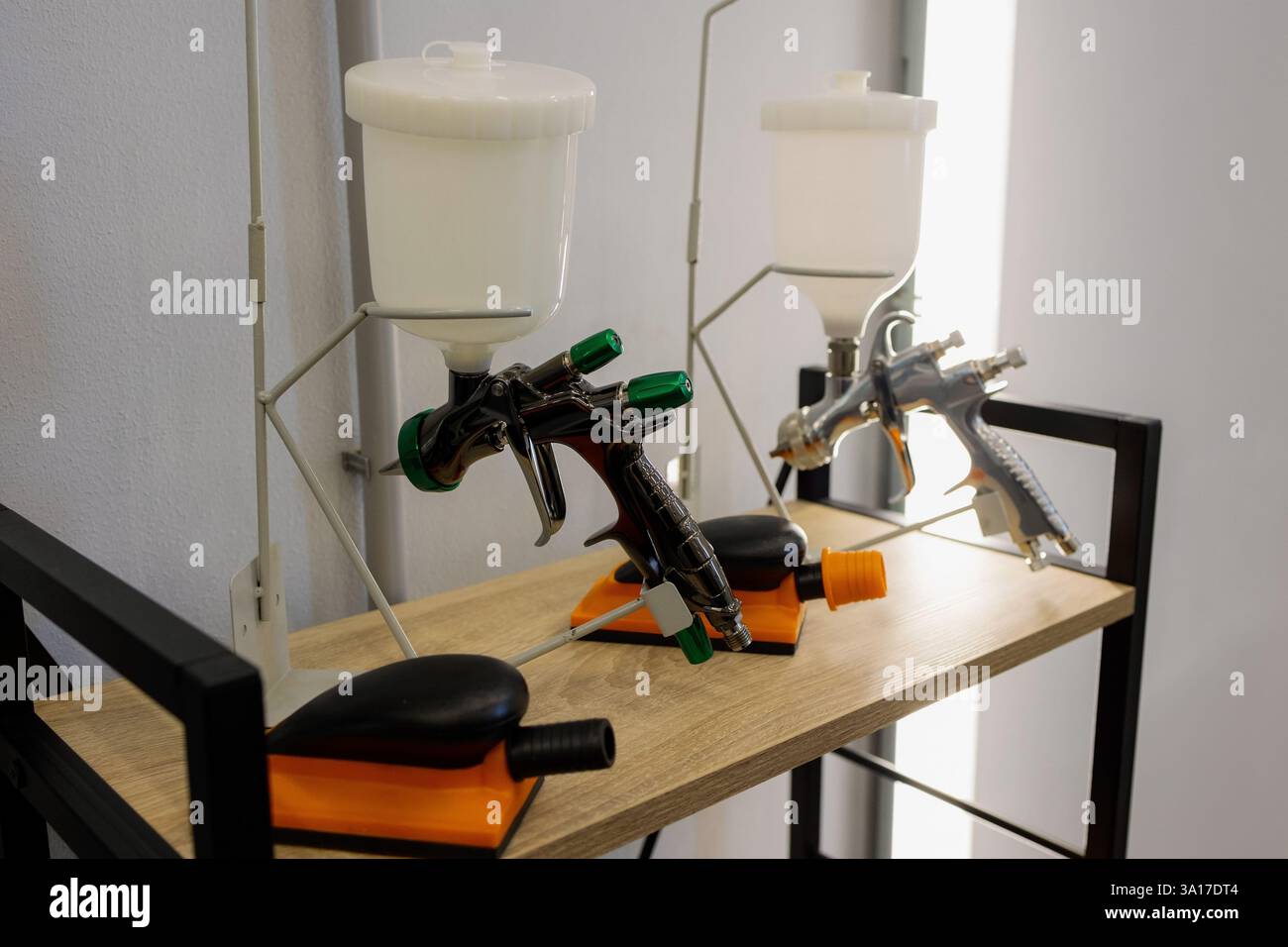 In un'elegante area di lavoro piena di luce, due pistole a spruzzo sono posizionate su un ripiano in legno, pronte per vivaci sessioni di pittura. Gli strumenti, completi di dolore Foto Stock