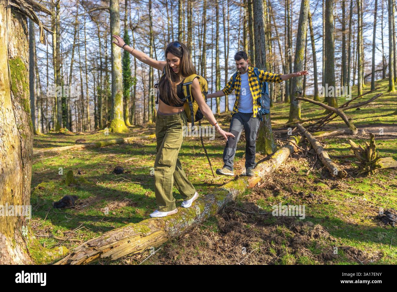 Escursionisti con zaini in equilibrio con cura su un tronco di albero caduto mentre si godono un'escursione attraverso una foresta soleggiata Foto Stock