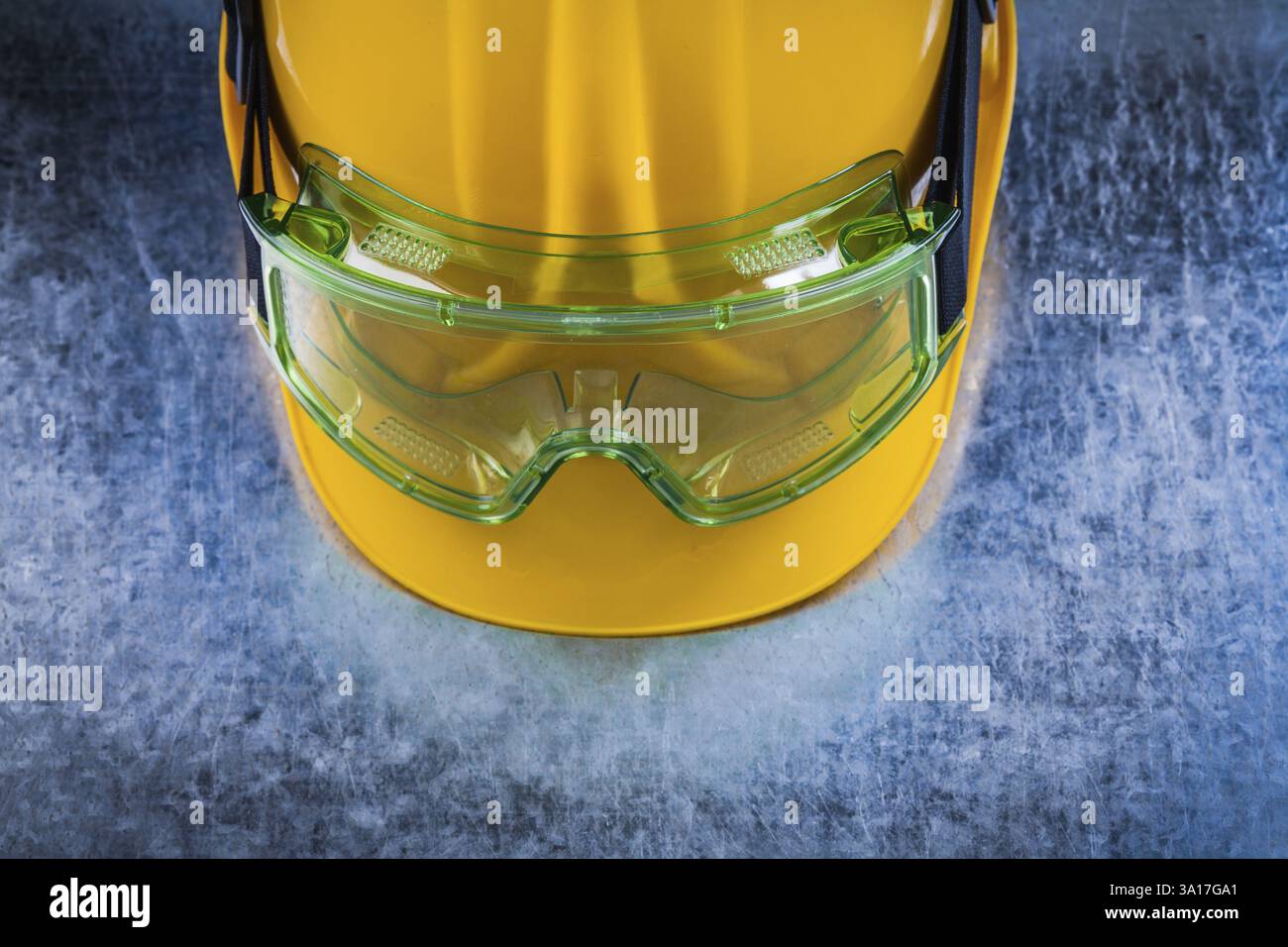 Vista ravvicinata del casco da costruzione e degli occhiali protettivi trasparenti su fondo metallico graffiato Foto Stock