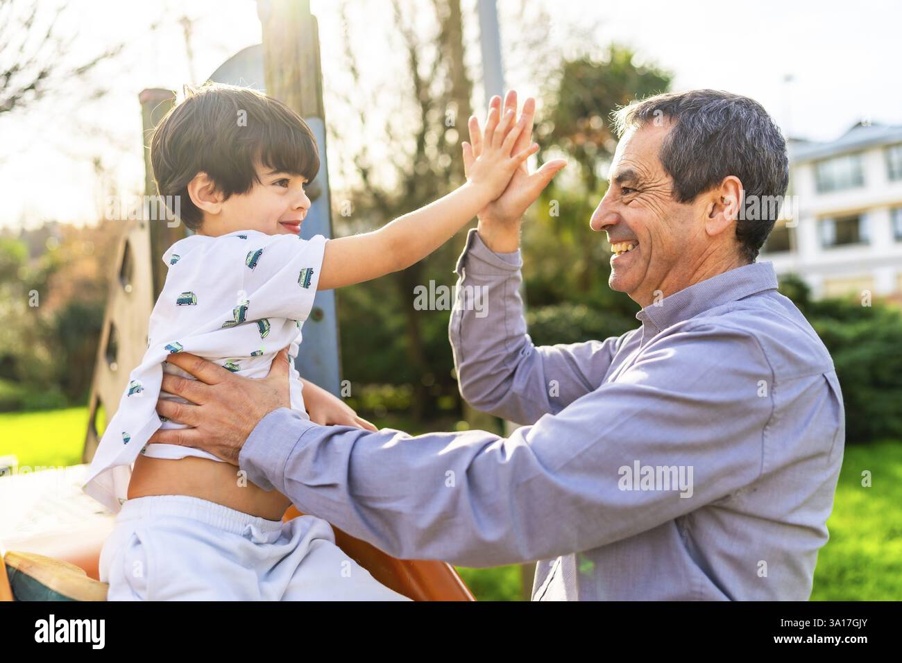 Nonno e nipote si divertono insieme al parco giochi, dando un cinque alto e sorridendo Foto Stock