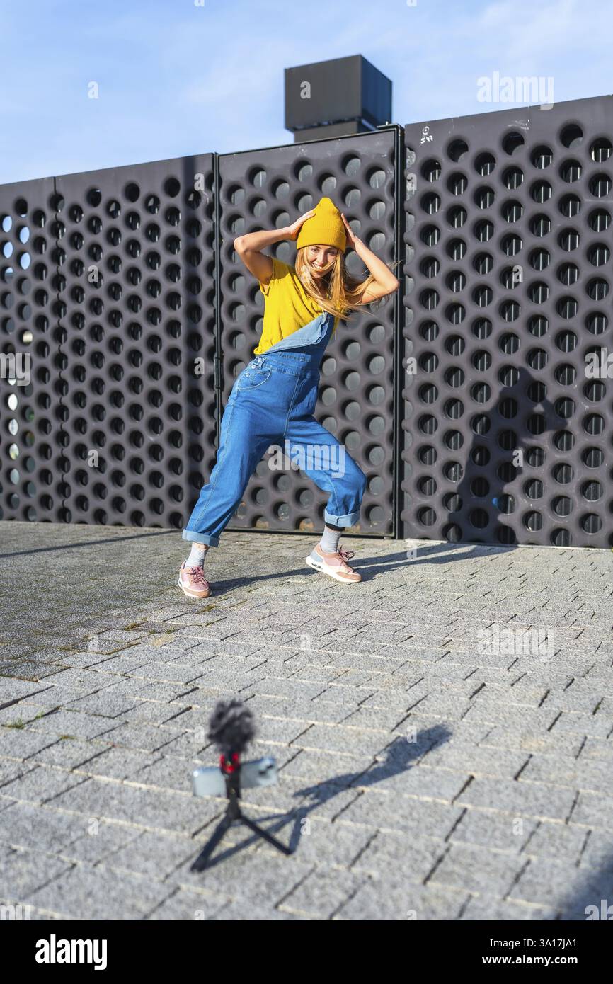 Influencer che crea contenuti video danzanti per i social media utilizzando smartphone e microfono esterno Foto Stock