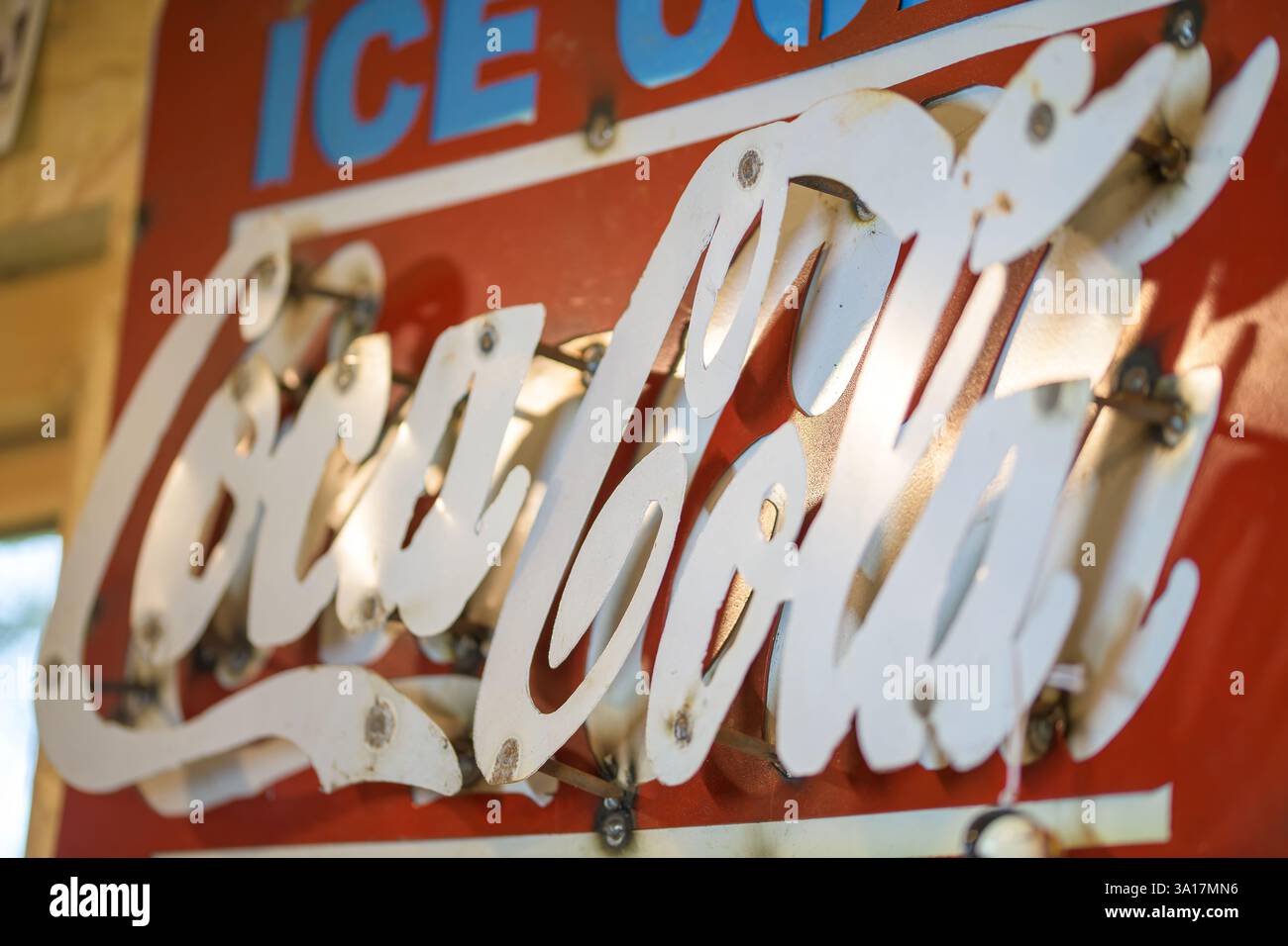 Insegna vintage in metallo Coca-Cola con lettere in stile "Distressed" in un ambiente all'aperto, con la luce riflessa dalla superficie metallica Foto Stock