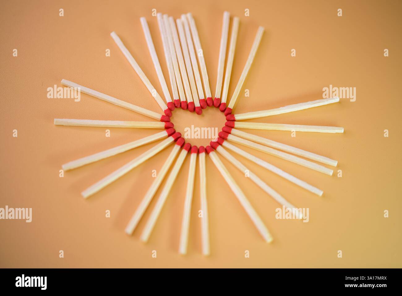 Disposizione a forma di cuore di fiammiferi dalla punta rossa circondata da un motivo circolare su un caldo sfondo beige neutro, amore, calore, che accende l'amore Foto Stock