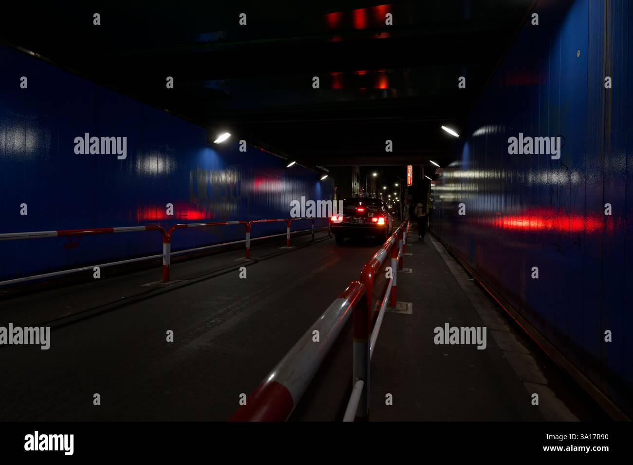 Il taxi solitario naviga in un sottopassaggio poco illuminato di Shinjuku, con le sue luci posteriori che emettono riflessi fugaci sulle pareti Foto Stock