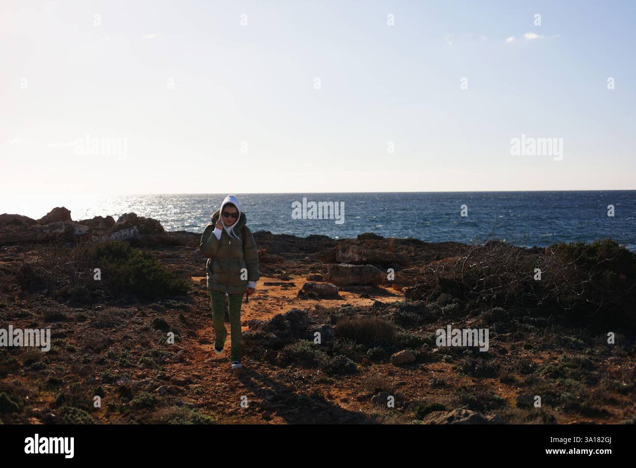 la ragazza che viaggia in abiti caldi cammina lungo il sentiero lungo la costa del mare. viaggio da solo. la ragazza sorride, l'uomo felice si rallegra Foto Stock