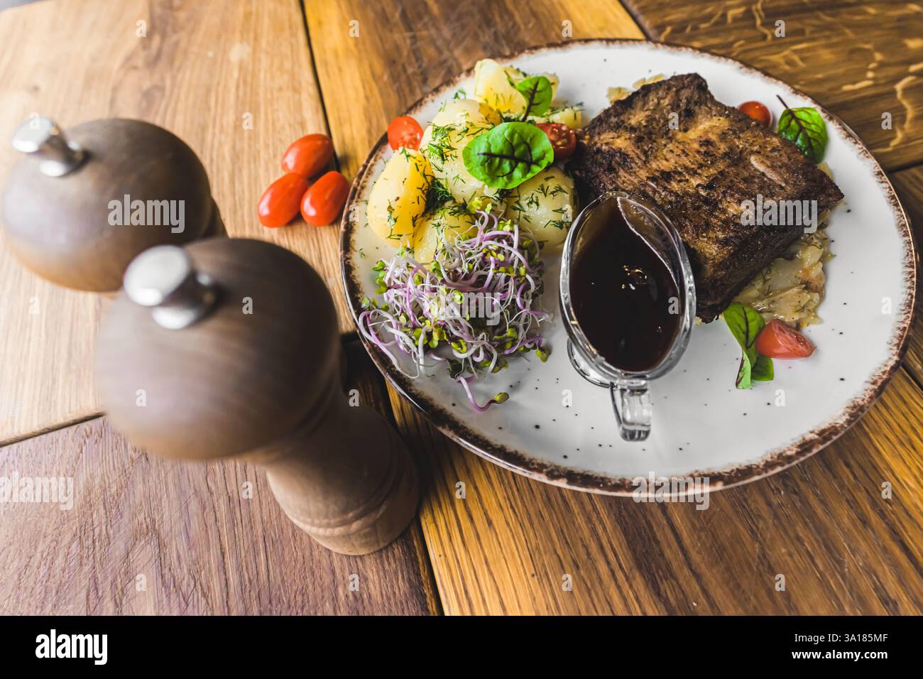 Primo piano di un saporito piatto fatto in casa con carne alla griglia, verdure vivaci e patate bollite condite, splendidamente placcate su un rustico tavolo in legno in un ambiente accogliente e invitante. Foto Stock