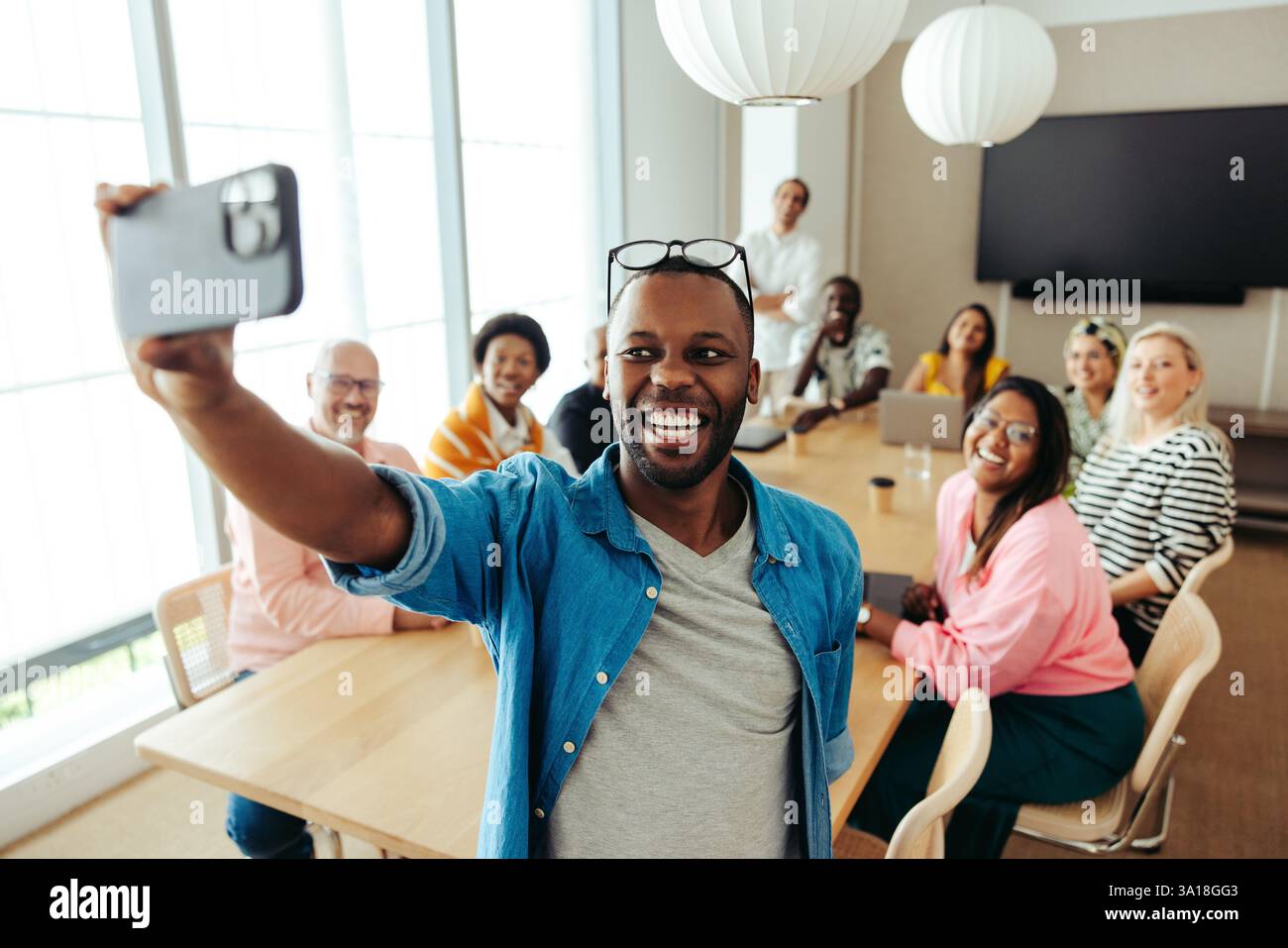 Un gruppo di colleghi d'affari sorridenti di diversa provenienza, che scattano un gioioso selfie durante una riunione d'ufficio. L'immagine mostra il lavoro di squadra, diversi Foto Stock
