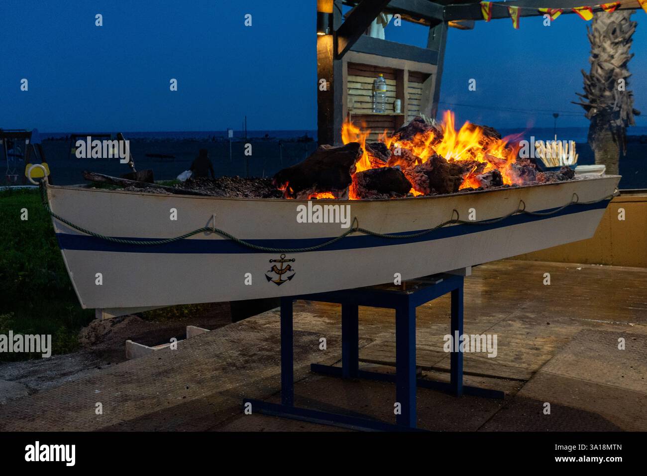 Un'imbarcazione riproposta piena di carboni caldi ardenti rende un barbecue unico e accattivante all'aperto di notte, pronto per cucinare il cibo. Foto Stock
