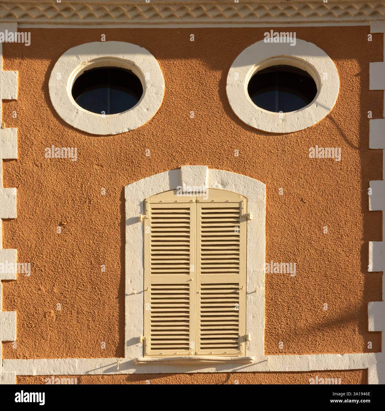 L'edificio arancione luminoso presenta due finestre circolari e una tapparella di legno sotto di esse, che creano un aspetto stravagante simile a una faccia contro un cielo limpido Foto Stock