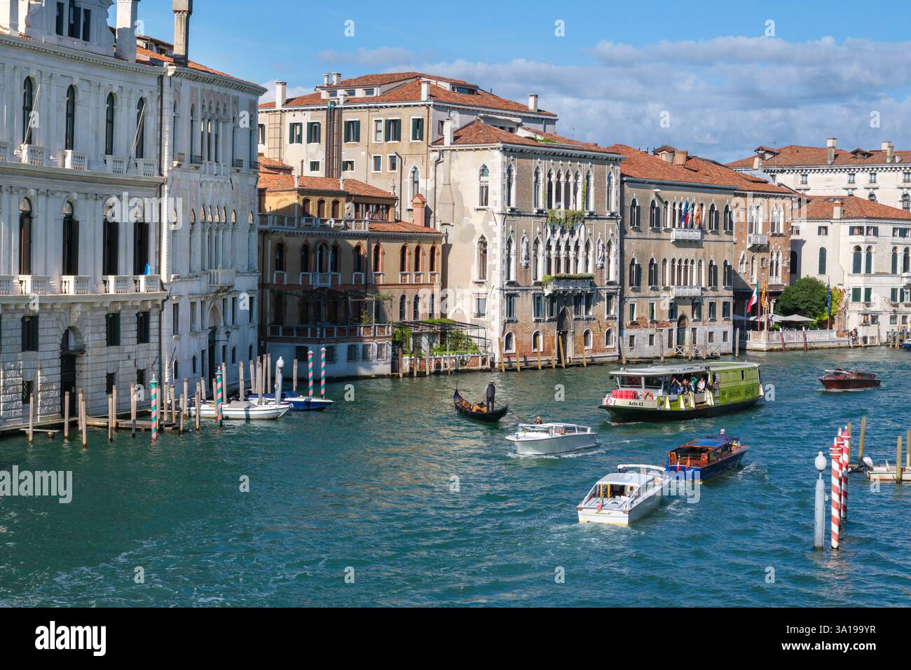 Venezia, Italia - 12 ottobre 2024: Barche, gondole e un vaporetto navigano sul Canal grande, circondato da storici palazzi veneziani sotto un luminoso blu Foto Stock