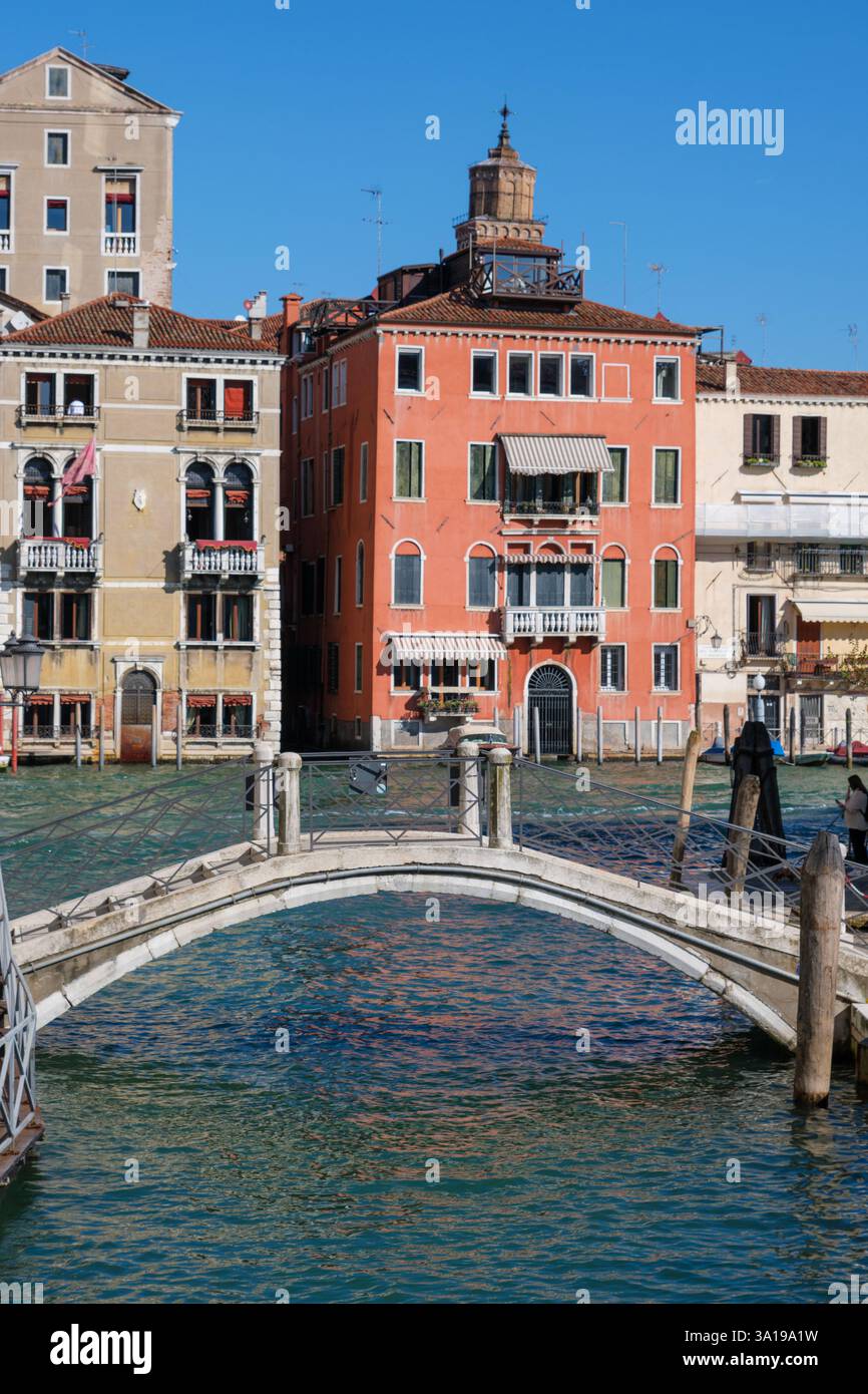 Venezia, Italia - 12 ottobre 2024: Un piccolo ponte pedonale attraversa un canale veneziano, circondato da colorati edifici storici sotto un cielo azzurro Foto Stock