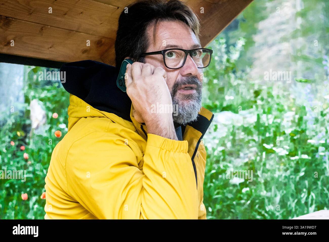 Viaggiatore maturo che parla durante una telefonata all'aperto e lavora in un ufficio alternativo con un computer portatile e una bottiglia di caffè. Le persone viaggiano con stile di vita e svolgono attività di lavoro a distanza. Divertimento in montagna Foto Stock