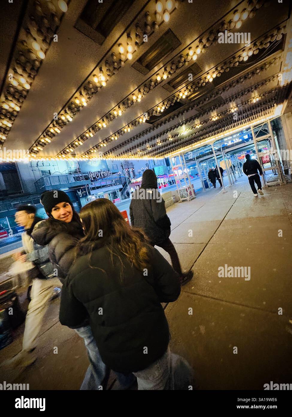 Persone non identificate che camminano sotto i segni al neon degli spettacoli di broadway a New York City, New York - Immagine stock catturata con smartphone