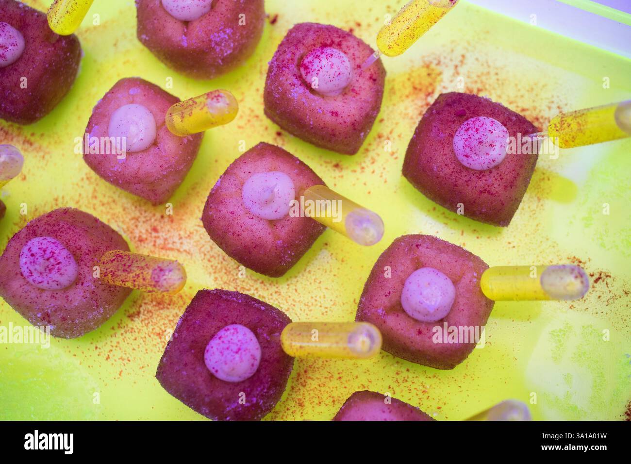 Piccoli dessert rosa quadrati con centri crema bianca, guarniti con spruzzette rosa, sono serviti su un vassoio giallo lime Foto Stock