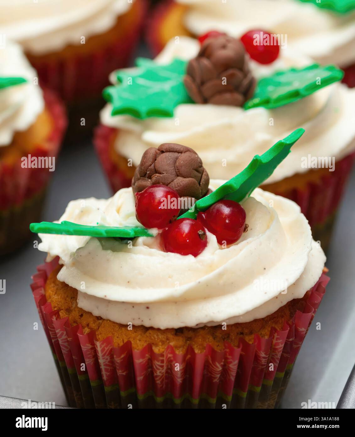 Cupcake natalizi con glassa bianca, decorati con bacche rosse, coni di pino al cioccolato e foglie di agrifoglio ti aspettano su un vassoio per la festa di natale Foto Stock