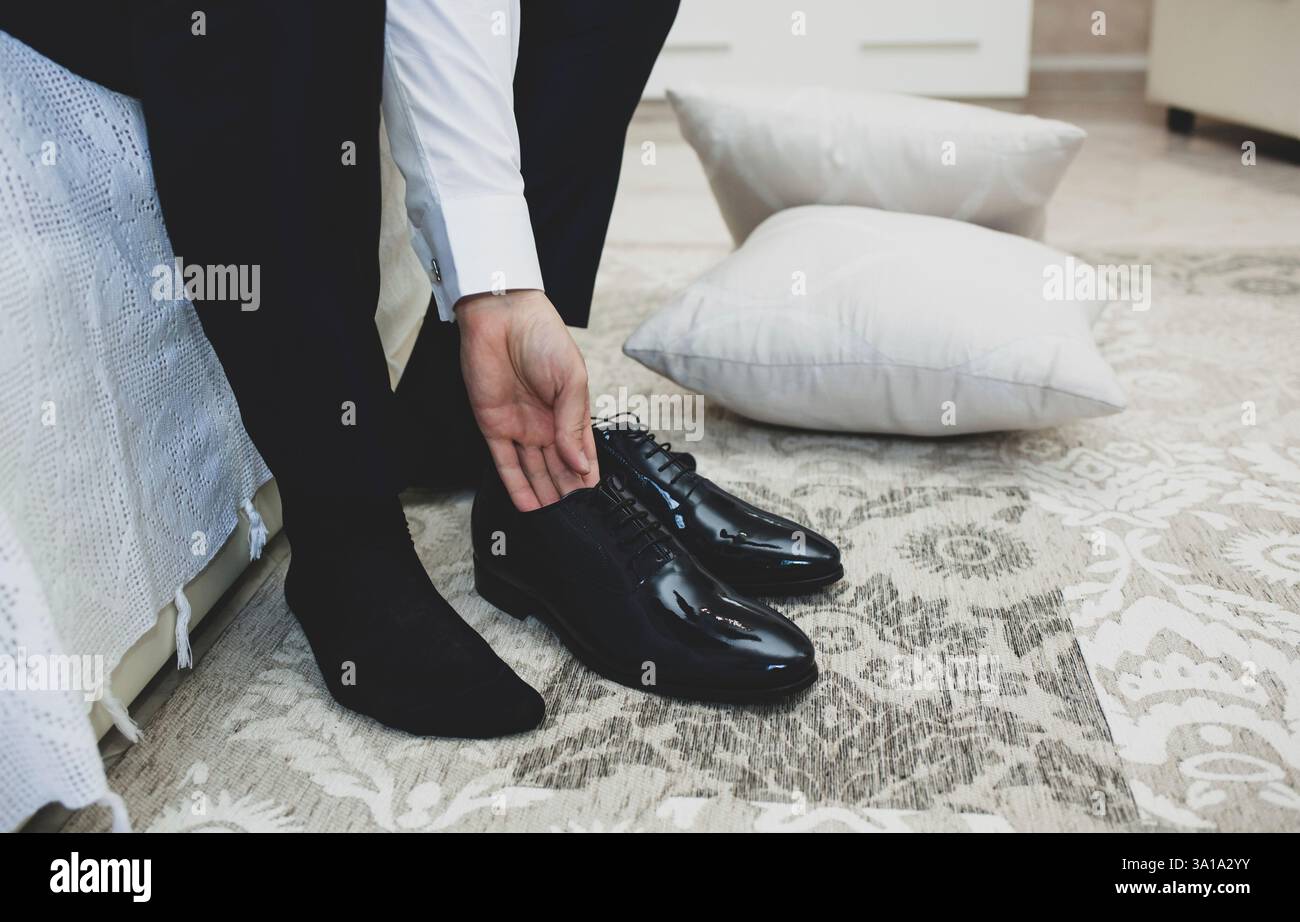 Un uomo in un vestito si lega a lacci delle scarpe su nero classico ed elegante scarpe. Lo sposo mattina in camera in hotel prima di cerimonia nuziale. Foto Stock