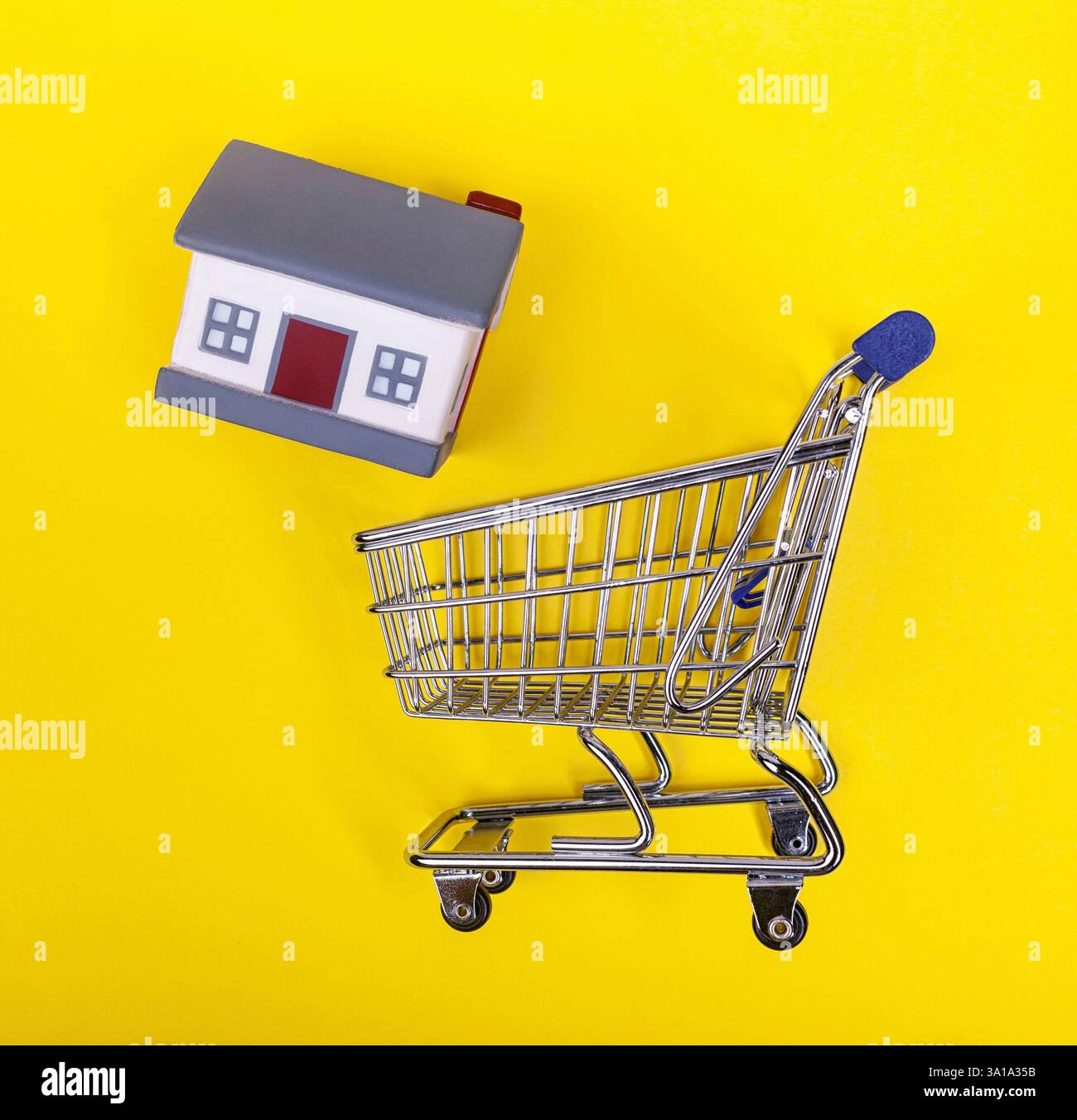 Un carrello per supermercati con case in gomma su sfondo giallo. Il concetto di home shopping e marketing, commercio e. Foto Stock