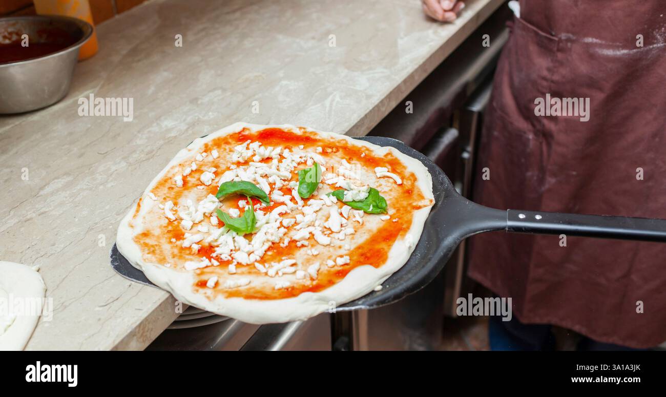 Materie pizza margherita messo sulla pala da forno per la cottura. Foto Stock