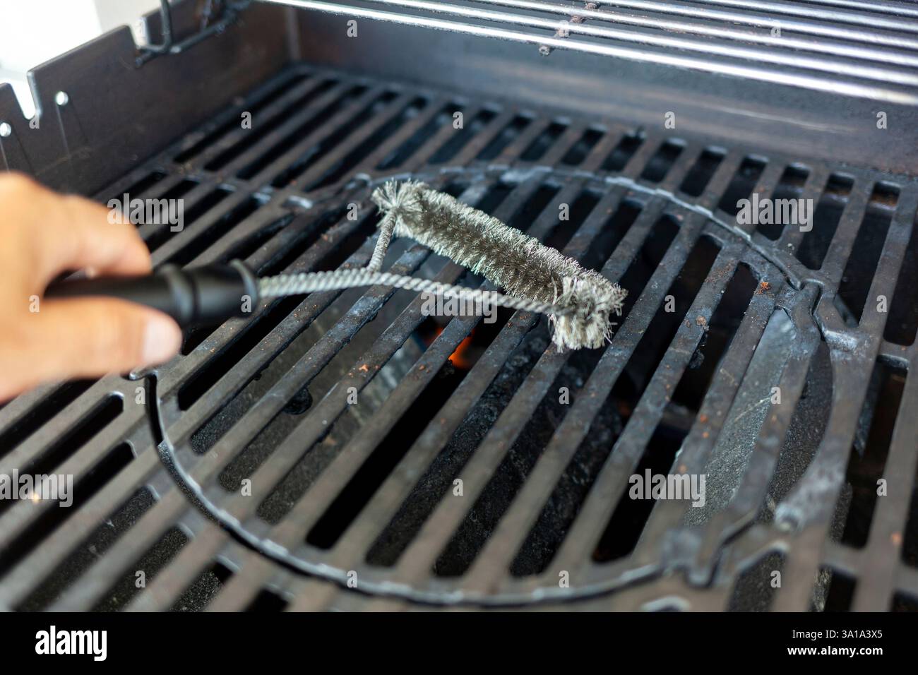 La persona sta pulendo una griglia per barbecue con una spazzola metallica Foto Stock