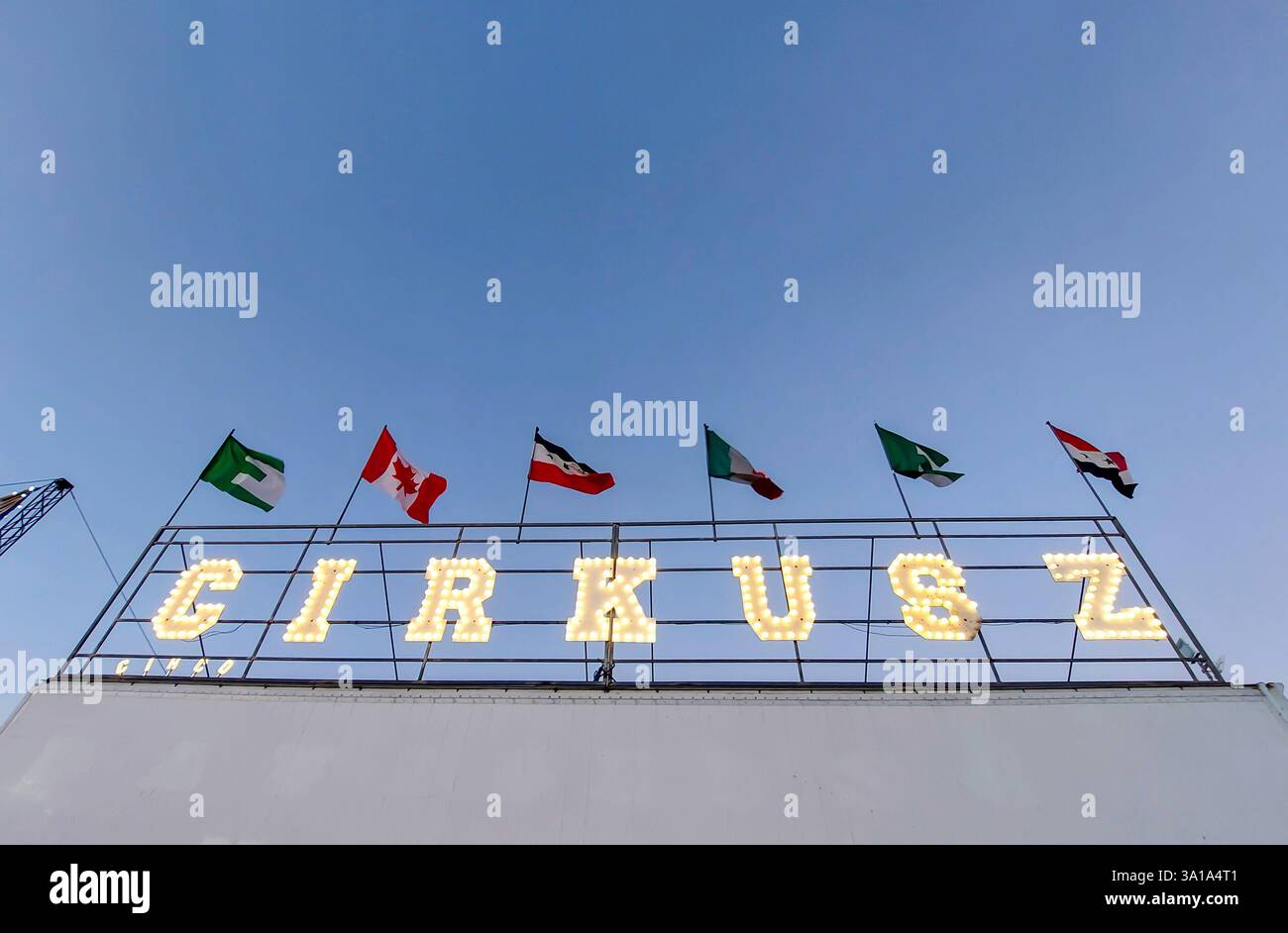 Insegna di Cirkusz con bandiere internazionali illuminate e sventolate nel vento, adagiata su un cielo blu vibrante Foto Stock