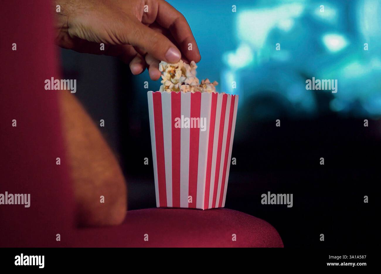 Mangiare popcorn mentre si guarda un film sul divano a casa. Scena in una casa con luci luminose, una notte di film con il profumo di pop corn. Foto Stock