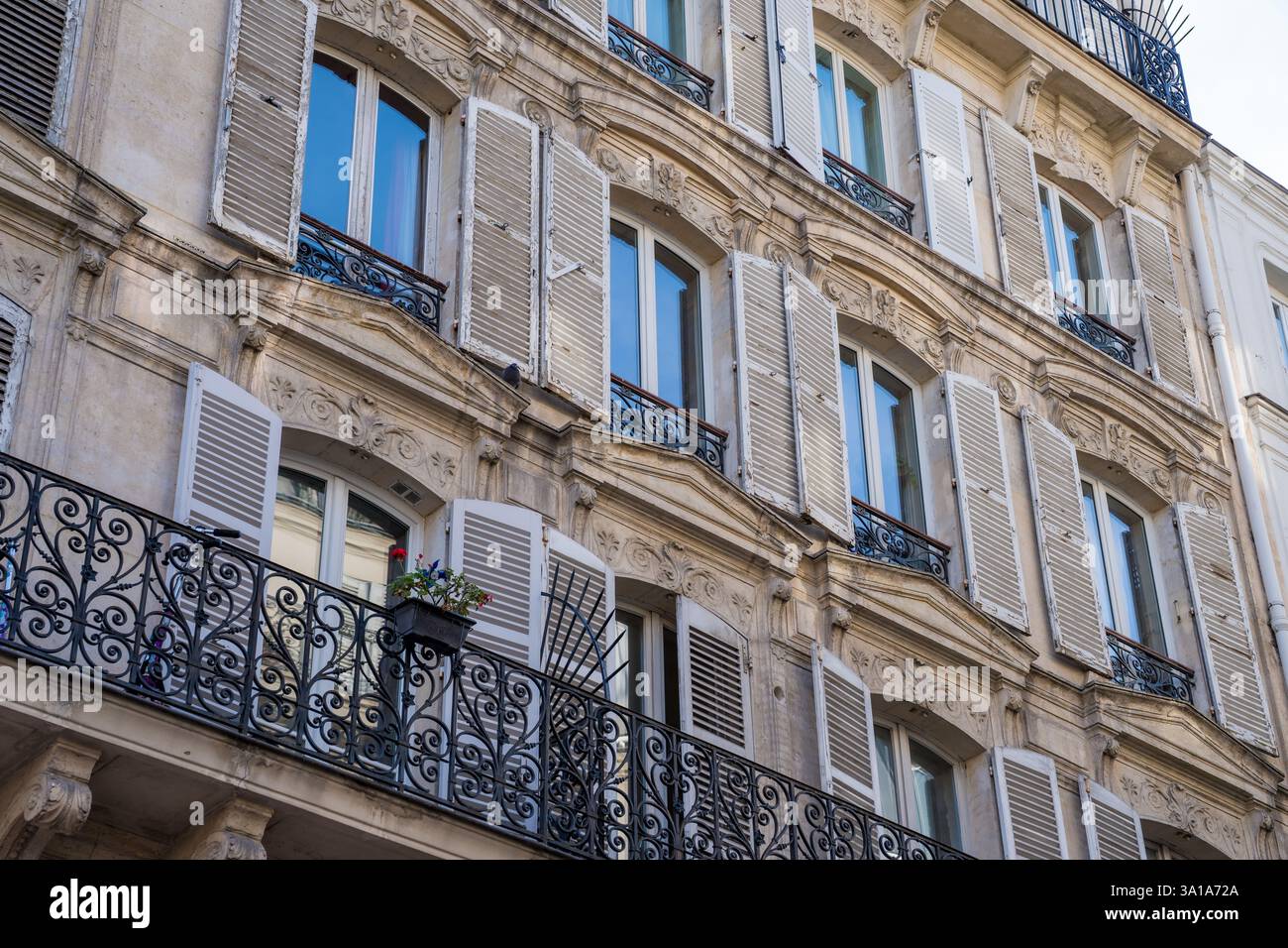 L'elegante architettura parigina mette in mostra dettagli intricati e balconi adornati con piante in vaso alla luce del sole pomeridiano Foto Stock